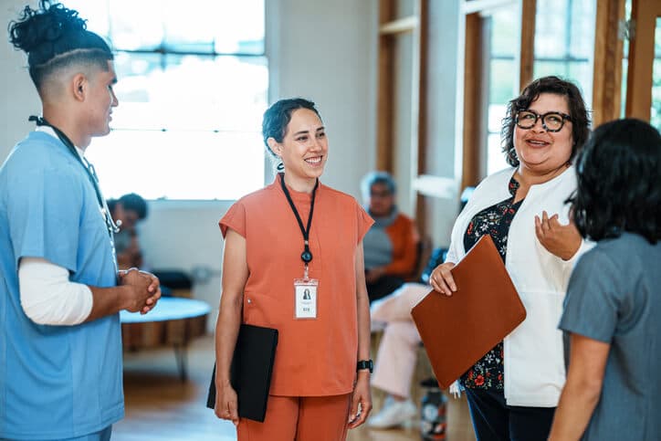Female public health professional listens intently to her coworkers during a meeting in a hospital corridor.