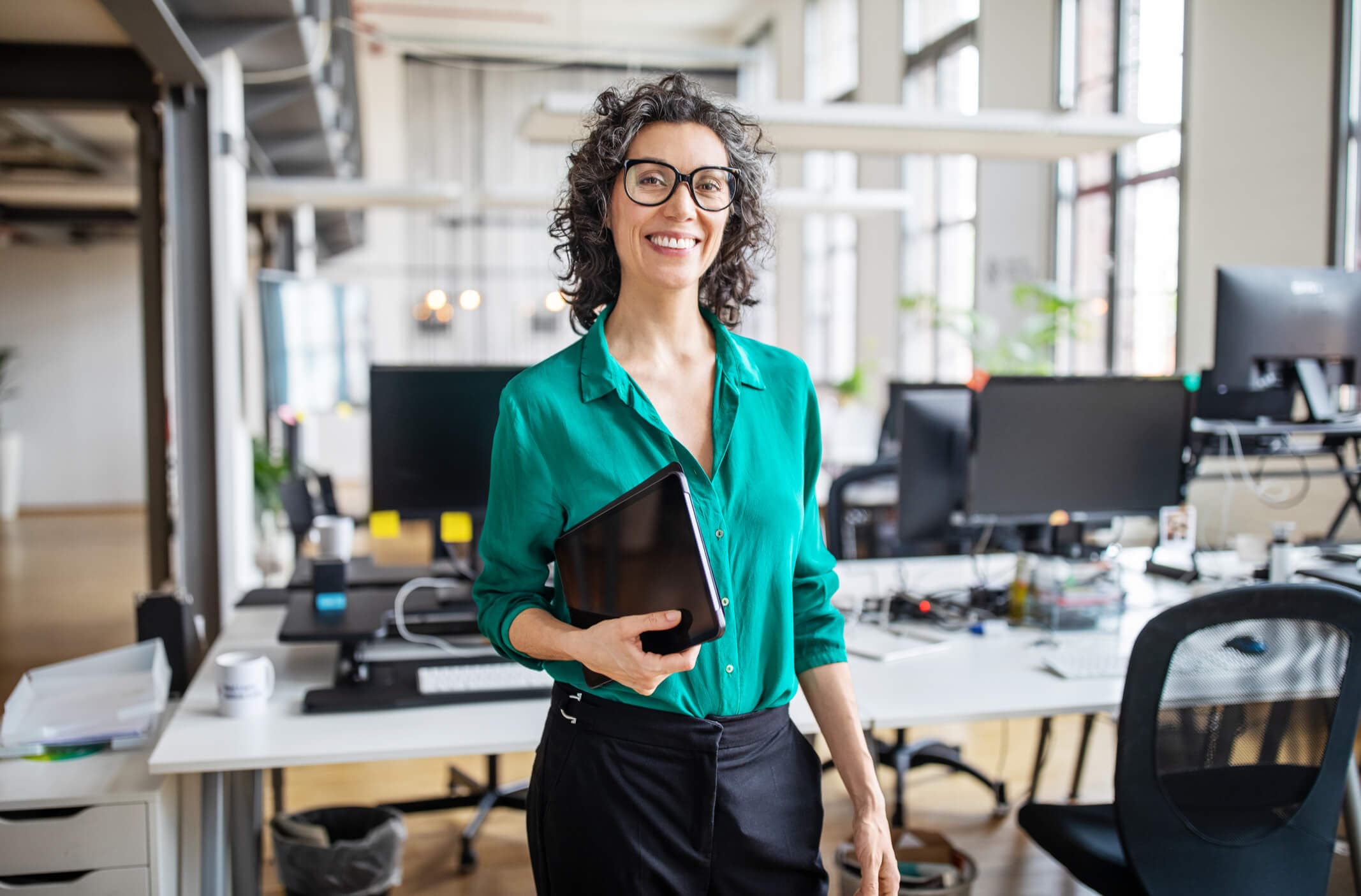 Portrait of mature businesswoman in casuals standing at her desk with digital tablet.