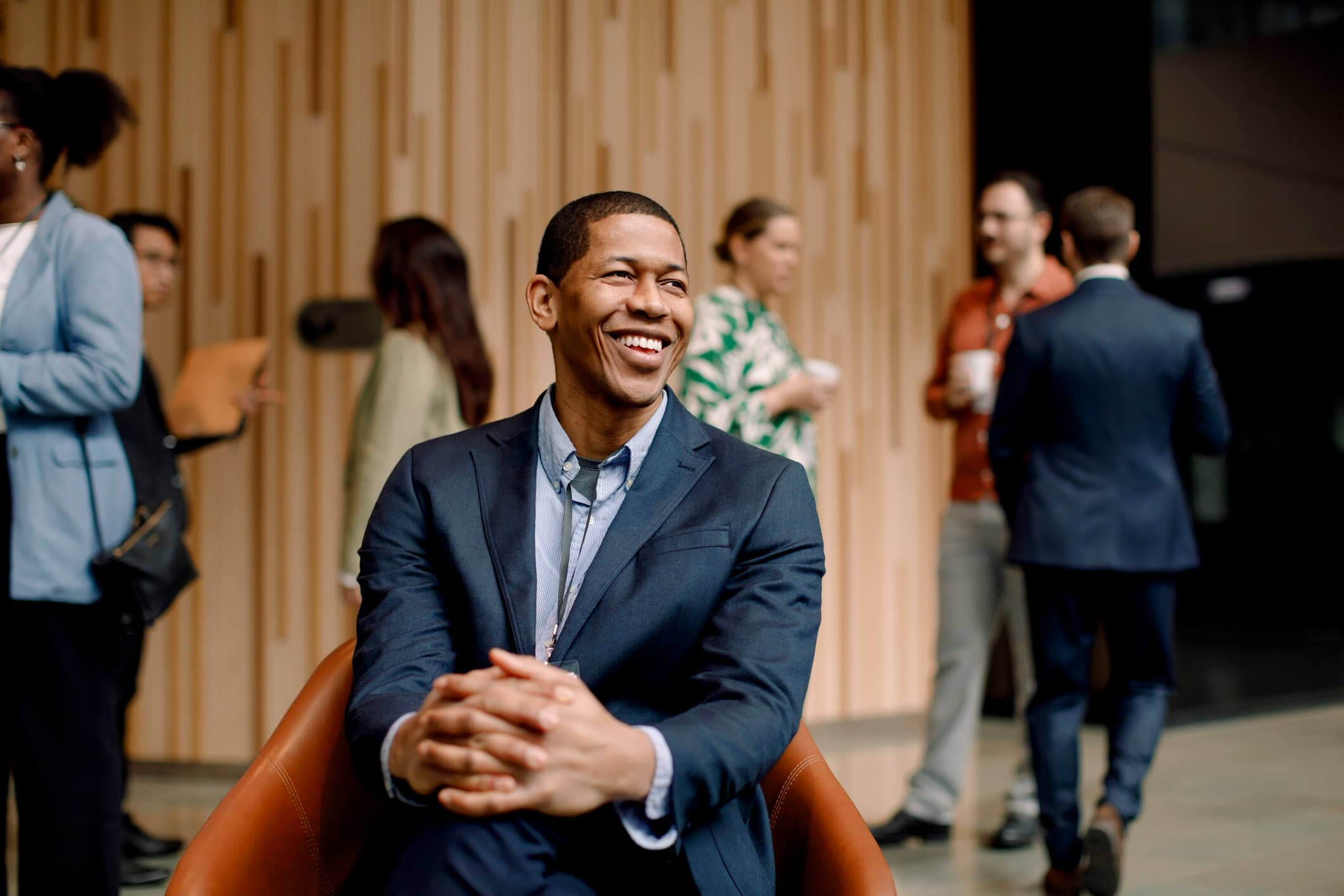 Smiling male global business entrepreneur sitting on a chair with his hands intertwined at a convention center.