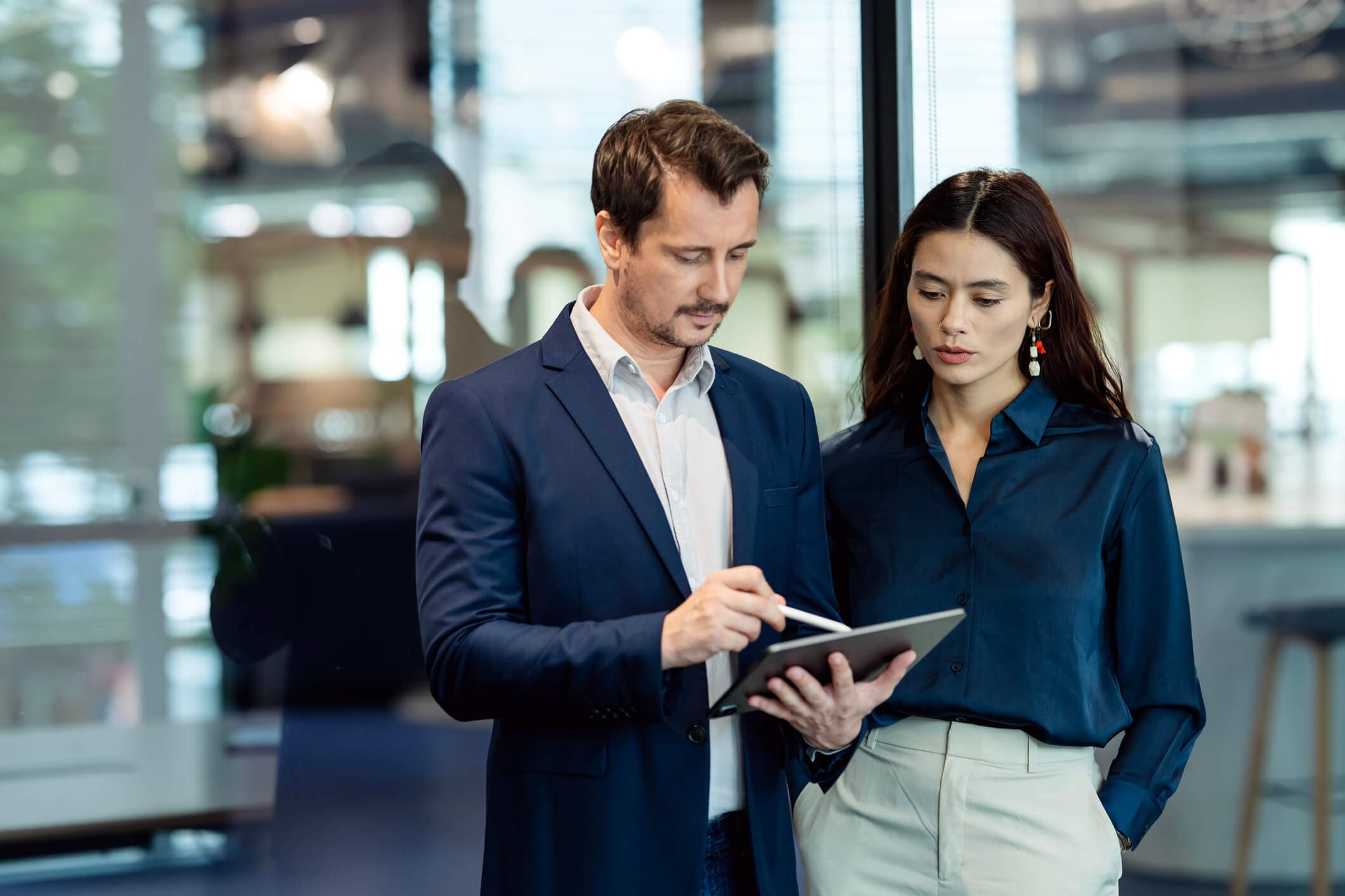 Reviewing real-time business data on a tablet, a multi-ethnic business development team in a modern business and technology office is evaluating the effectiveness of their business processes to refine their strategies.