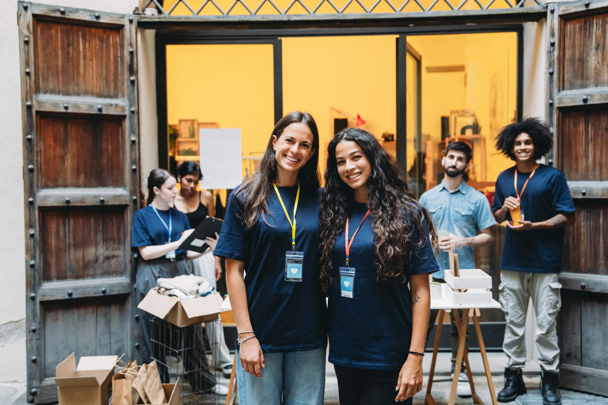 Two young female volunteers smiling at the camera while working for a charity, organizing donations.