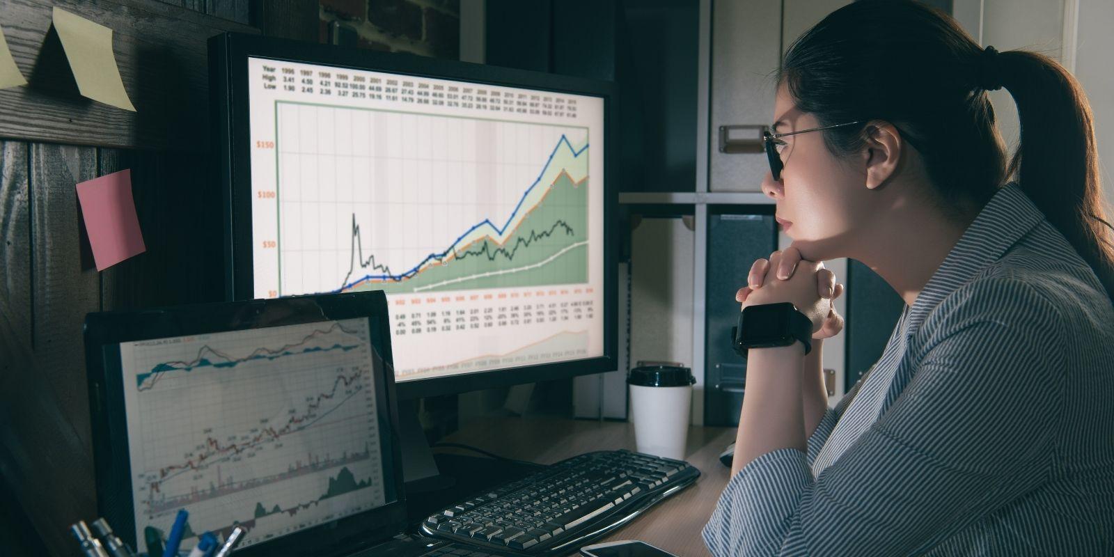 Asian American woman looking at a series of line charts with financial analysis figures on her desktop computer.