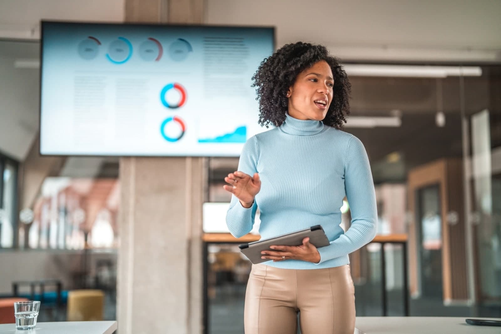 woman in front of a screen showcasing data while giving leading a discussion.
